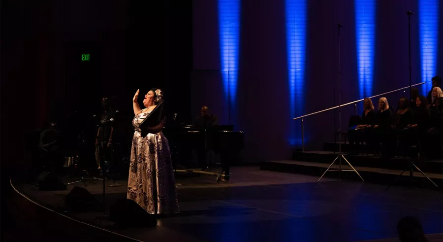 Thomasina Petrus performing a solo with columns of blue light in the background.