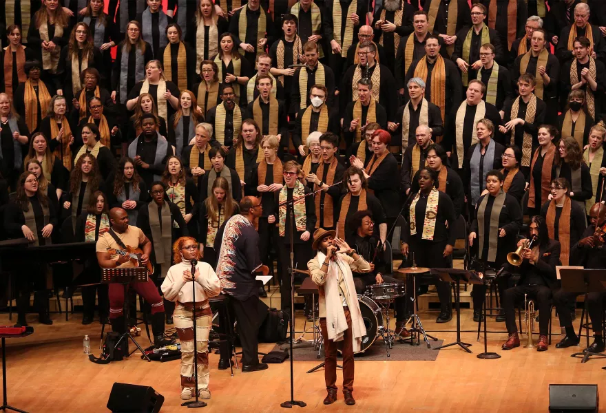 Two soloists at mics with the VocalEssence chorus behind them on risers.