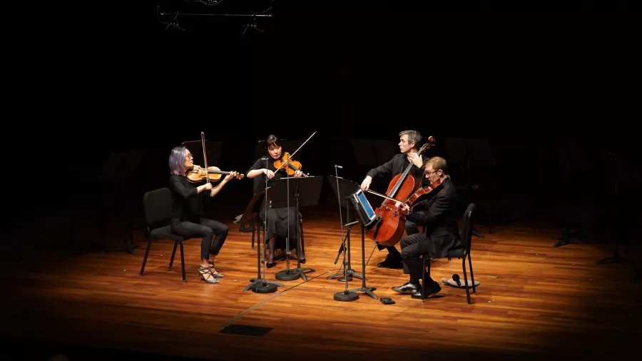 Four members of the Saint Paul Chamber Orchestra sit in a half-circle playing their string instruments on a stage