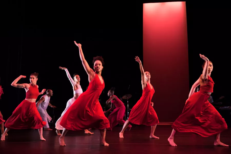 A group of dancers in red dresses perform on stage.