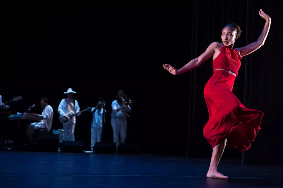 A female dancer performs on stage with as a band plays in the background.