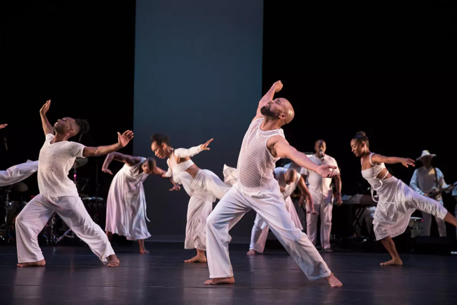 A group of dancers wearing all white perform on stage.