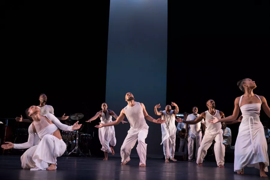 A group of dancers wearing all white perform on stage.