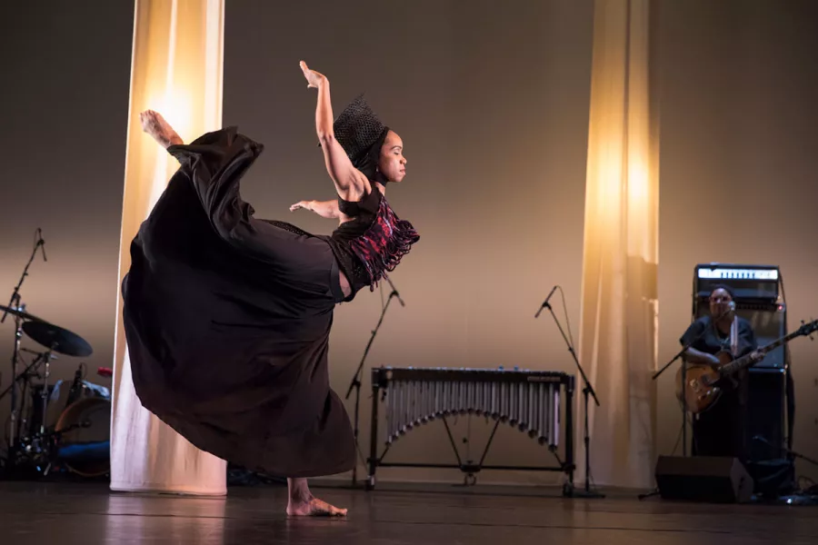 A female dancer poses on stage with lit columns behind her.