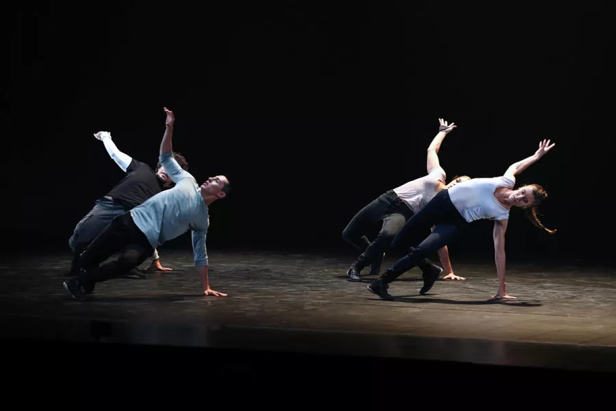 Four dancers in formation arching to the side with one hand on the ground the other reaching up and back