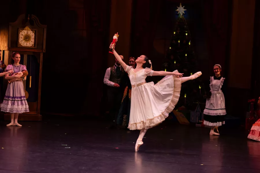 Dancer in long dress arabesques while holding up a toy nutcracker