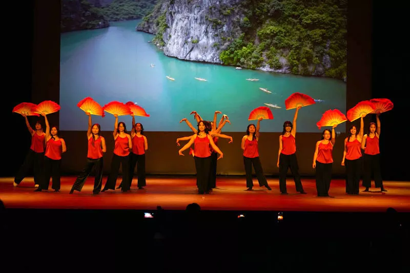 Dancers in red tops and black pants dance with traditional hand fans