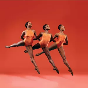 Three female dancers perform together in front of an orange background.